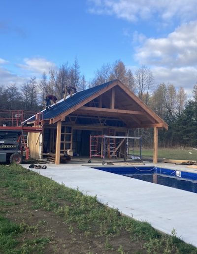 High-quality timber frame building under construction near poolside. Skilled craftsmen building custom pool houses with timber.